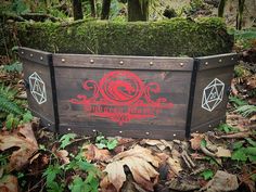 a wooden box sitting in the middle of some leaves and plants with an iron dragon logo on it