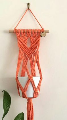 an orange macrame hanging from a white wall next to a potted plant