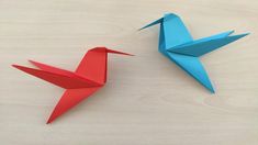 two origami birds sitting next to each other on a wooden surface, one red and one blue