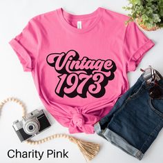 Celebrate decades of awesomeness with our timeless "Vintage 1973" T-shirt! This design is a tribute to the incredible journey of being awesome for nearly five decades. Carefully crafted with comfort in mind, this t-shirt is made from high-quality, soft cotton fabric that feels great against your skin. The classic unisex design ensures a flattering fit for both men and women, while the bold "Vintage 1973" phrase adds a touch of retro charm to any outfit. Whether you're celebrating your own birth Vintage Cotton Tops For Anniversary, Retro Short Sleeve T-shirt For Birthday, Vintage Custom Print T-shirt For Fan Merchandise, Vintage Letter Print Tops For Anniversary, Retro Graphic Print Tops For Anniversary, Vintage Short Sleeve Tops For Birthday, Vintage Text Print Top For Birthday, Retro Letter Print Tops For Birthday, Vintage Graphic Print Top For Birthday