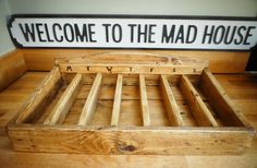 a wooden bed frame sitting on top of a hard wood floor next to a sign that says welcome to the mad house