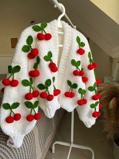 a white sweater with cherries on it hanging from a clothes rack next to a teddy bear