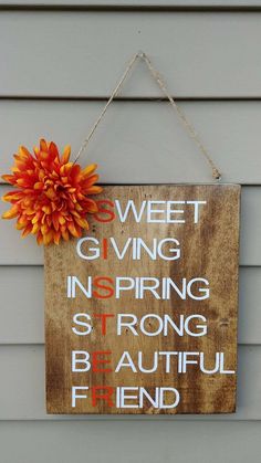 a wooden sign hanging on the side of a house with a flower in front of it