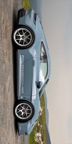 a blue sports car parked on the side of a road next to a body of water