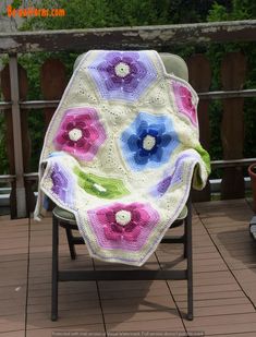 a crocheted blanket sitting on top of a lawn chair next to a wooden fence