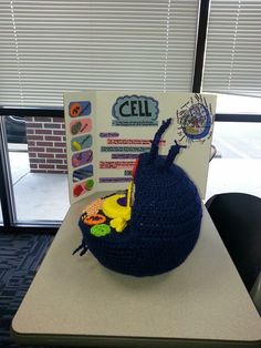 a crocheted hat sitting on top of a desk next to a sign that says cell