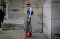 a woman standing in front of a stone wall wearing red boots and a plaid dress