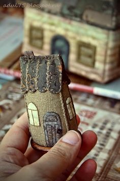 a hand holding a small doll house made out of burlocked fabric and paper