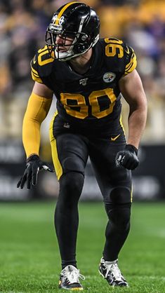 a football player standing on top of a field wearing a black uniform and yellow gloves