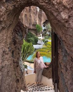 a woman is standing in an archway between two stone buildings with plants on the other side