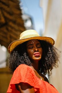 a woman in an orange dress and straw hat looks off to the side with her eyes closed