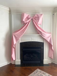 a fireplace with a pink bow on it's mantle in a room that has white walls and wood floors