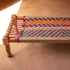 a close up of a wooden bench with multicolored weaving on it's back