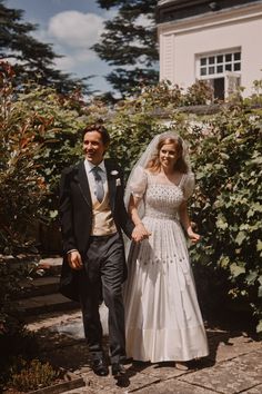 the bride and groom are walking together in front of some bushes with flowers on it