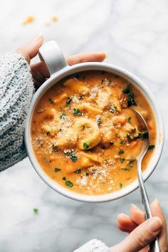 a person holding a bowl of soup with meat and cheese in it on a marble surface