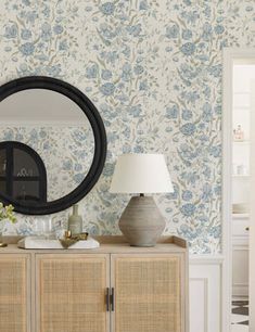 a living room with floral wallpaper and a large round mirror on the sideboard