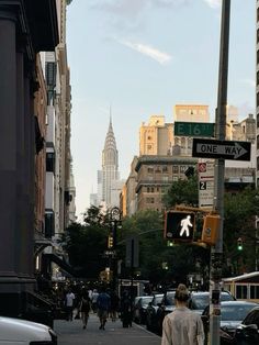 a man walking down a street next to traffic lights and tall buildings in the background