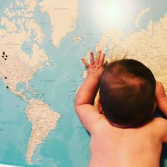 a baby is looking at the world map with his hands on it's head