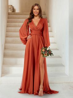 a woman in an orange dress standing on stairs with her legs crossed and holding a bouquet