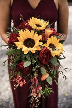 a woman holding a bouquet of sunflowers and red roses in her hands,