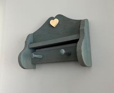 a wooden shelf with a heart on the top and two hooks attached to it, against a white wall