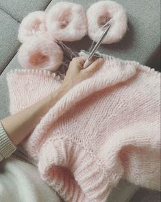 a person cutting yarn with scissors on top of a gray couch next to pink flowers