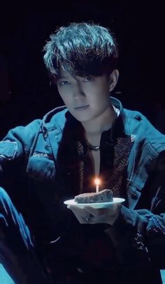 a young man holding a plate with a lit candle in it's hand and looking at the camera