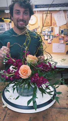 a man is holding flowers in a vase on a table with other items around him