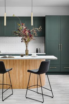 two bar stools sit in front of a kitchen island with green cabinets and marble countertops