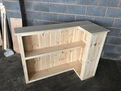 a wooden shelf sitting on top of a floor next to a brick wall in a garage