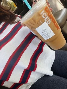 a woman holding up a cup of iced coffee in her hand while sitting on the back seat of a car