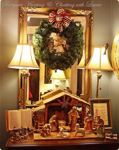 a nativity scene is displayed in front of a christmas wreath and two lamps on a table