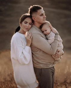 a man and woman holding a baby in their arms while standing in the middle of a field