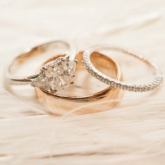 two wedding rings sitting next to each other on top of a white furnishing