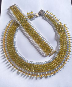 "Double Sided Yellow and Silver Statement Necklace and Bracelet - Yellow and Silver Regal Lace Bib Necklace and Bracelet - Yellow and Silver Crystal Necklace and Bracelet Beautiful and elegant handmade crystal and seed bead flat necklace in Regal Lace style necklace. The necklace is double layered. It is composed of silver, teal and white glass seed beads. The necklace also has yellow crystal type glass beads. Connector clasp is in antique gold toned with diamond type insets. Matching bracelet double layered. It is composed of silver, teal and white glass seed beads as well as yellow crystal type glass beads. Slider clasp is gold toned with three hole connections. Bracelet is reversible and can be worn exposing either side. The width of the bracelet is 1 1/2\". Necklace Length from clasp t Yellow Jubilee Bracelet, Yellow Round Jewelry For Parties, Yellow Beaded Bracelet For Party, Yellow Bracelet Jewelry For Gift, Adjustable Yellow Bracelets With Lobster Clasp, Elegant Yellow Beaded Bracelets For Jewelry Making, Yellow Round Beads For Jewelry Making, Yellow Round Necklace For Party, Yellow Round Necklaces For Party