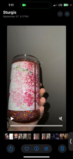 someone holding up a glass with pink flowers on it and glitter in the bottom half