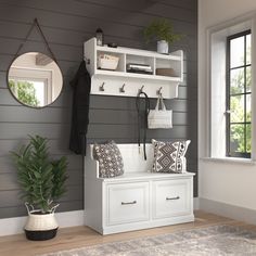 a white bench sitting under a window next to a mirror and potted plant on top of a wooden floor