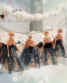 three skeletons dressed in black tulle skirts and white parasols are hanging from strings