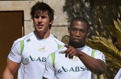 two men standing next to each other in front of a building with palm trees on the side