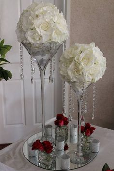 two wine glasses with flowers in them sitting on a table next to some silver cups