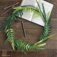 an open book on top of a wooden table next to a fern wreath and some twigs