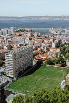 an aerial view of a soccer field in the middle of a city with water and buildings