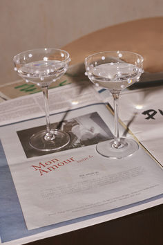 two martini glasses sitting on top of a table next to an article of news paper