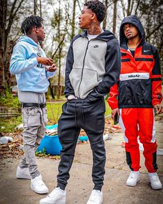 three young men standing next to each other in the woods, one wearing an orange and black hoodie