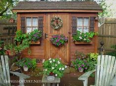 a small wooden shed with potted plants on the side and two lawn chairs in front