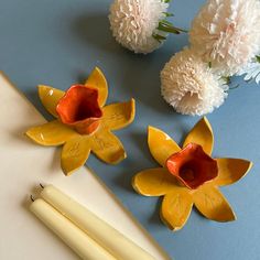 some flowers are sitting on a table next to two candles and one flower is in the middle