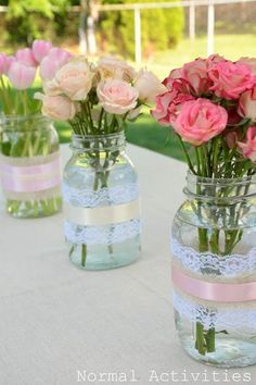 four vases with pink and white flowers in them on a table outside at a party