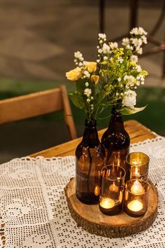 three brown bottles with candles are sitting on a wooden tray that has flowers in them