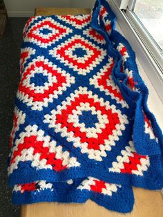 a crocheted blanket sitting on top of a wooden table next to a window