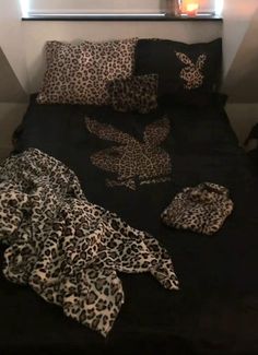 an unmade bed with leopard print sheets and pillows on it, next to a lit candle